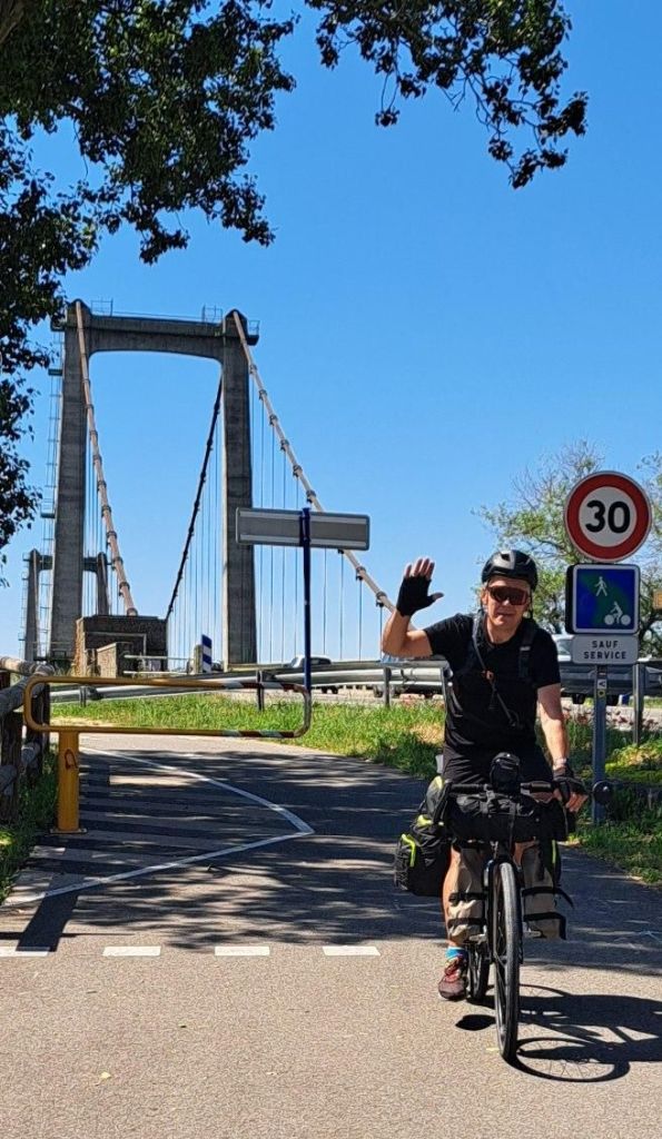 Stéphane à vélo, saluant devant un pont suspendu